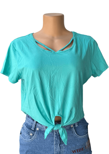 Vista de frente. Blusa corta verde con diseño amarrado en la parte delantera y detalles de tirantes cruzados en el escote.