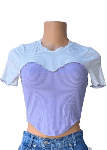 Vista de frente. Blusa corta bicolor con parte superior blanca y parte inferior morada, detalles ondulados en el borde.