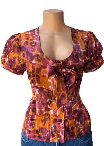 Vista de frente (una de dos). Blusa de manga corta con estampado tie-dye en tonos púrpura y naranja.