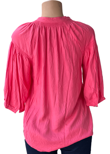 Vista de espalda (una de dos). Una blusa rosada de manga larga con botones frontales y un diseño holgado.