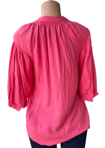 Vista de espalda (dos de dos). Una blusa rosada de manga larga con botones frontales y un diseño holgado.