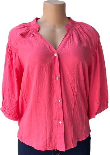Vista de frente (una de dos). Una blusa rosada de manga larga con botones frontales y un diseño holgado.