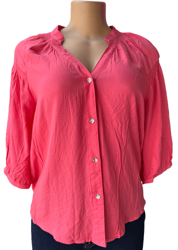 Vista de frente (dos de dos). Una blusa rosada de manga larga con botones frontales y un diseño holgado.
