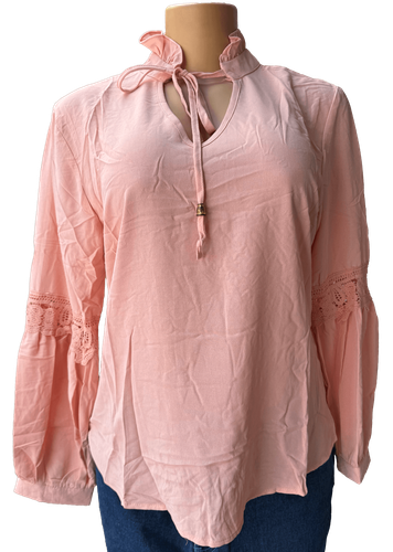 Vista de frente (una de dos). Una blusa salmón de manga larga con detalles de encaje en las mangas y un lazo decorativo en el cuello.