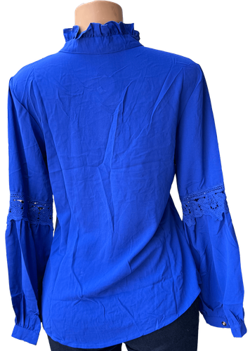 Vista de espalda (una de dos). Una blusa de manga larga azul con detalles de encaje en las mangas y cuello alto.