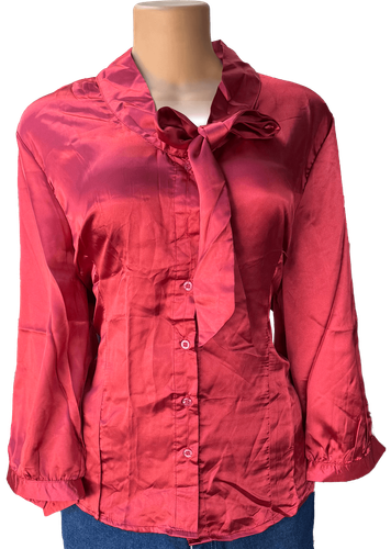 Vista de frente (una de dos). Blusa de satén con mangas largas y un diseño clásico de botones en la parte frontal y un lazo decorativo en el cuello.