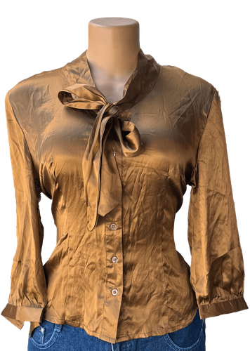 Vista de frente (una de dos). Blusa dorada con botones y lazo al cuello, manga larga.