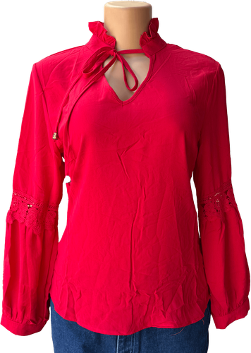 Vista de frente (una de dos). Blusa roja vibrante con cuello alto y diseño de encaje en las mangas, cierre de lazo en el cuello y detalle de volantes.